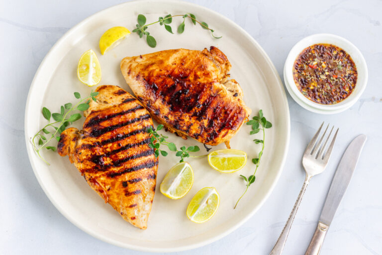 Grilled chicken breasts on a white plate with herbs and lemon slices