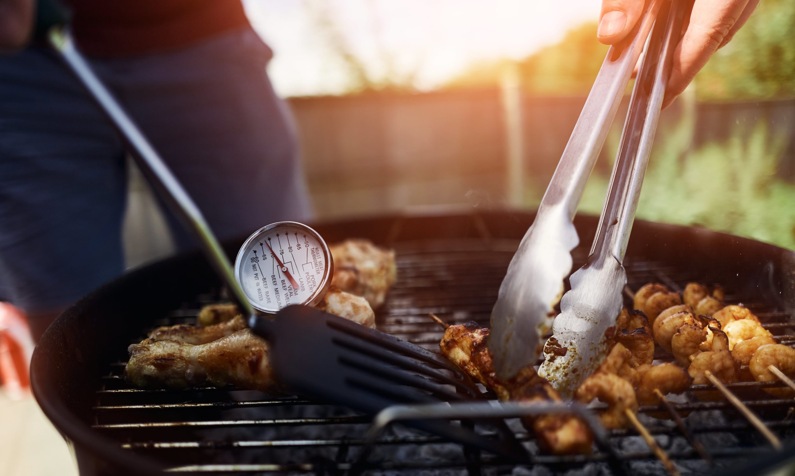 A food thermometer checking that chicken is being cooked correctly, safely on a BBQ on a sunny day in the garden.