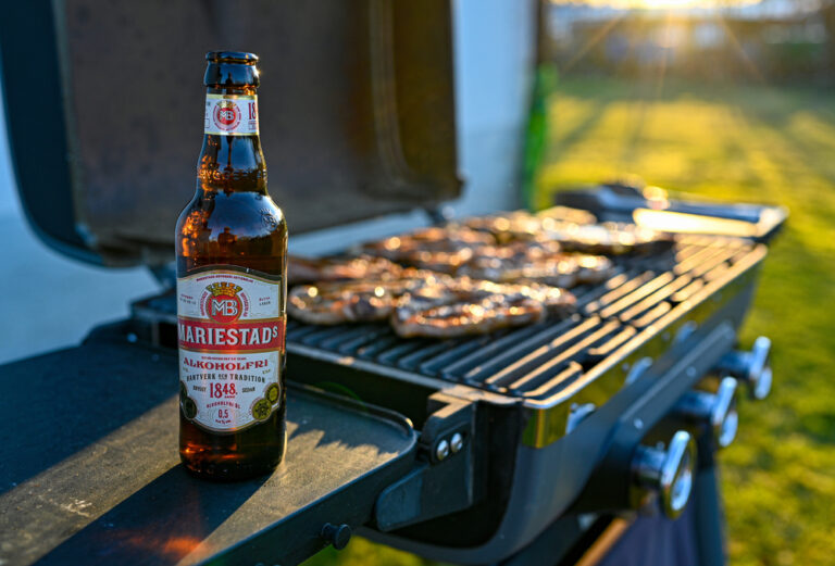 A picture of a beer next to a BBQ grill.