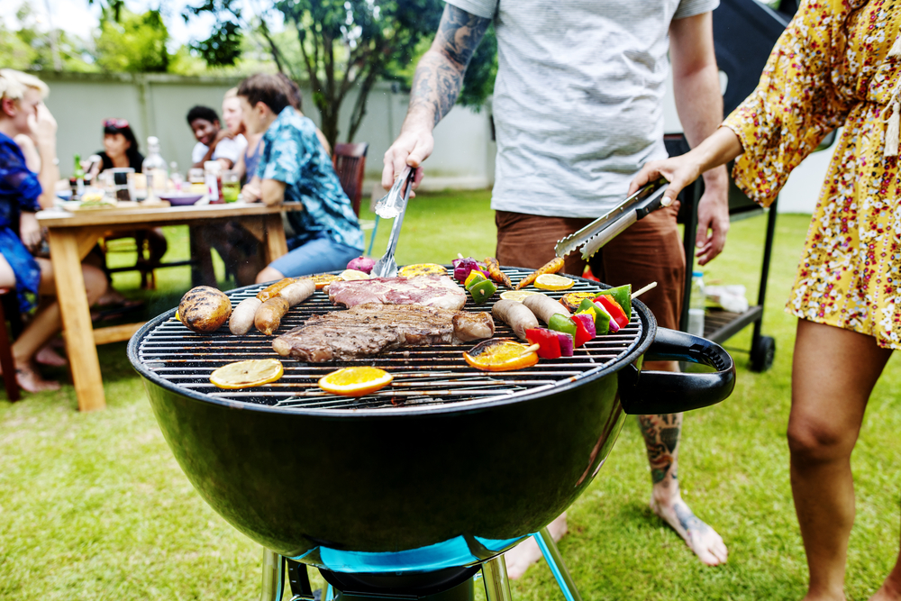 A picture of food on a BBQ with people in the background
